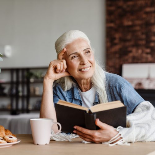 Smiling senior woman reading a book while sitting in the kitchen