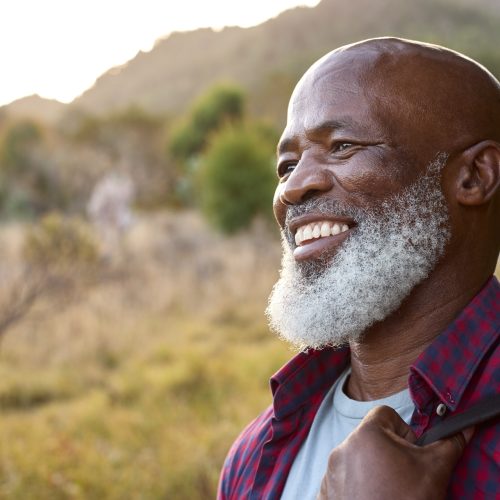 Close Up Portrait Of Active Senior Man With Backpack Hiking In Countryside