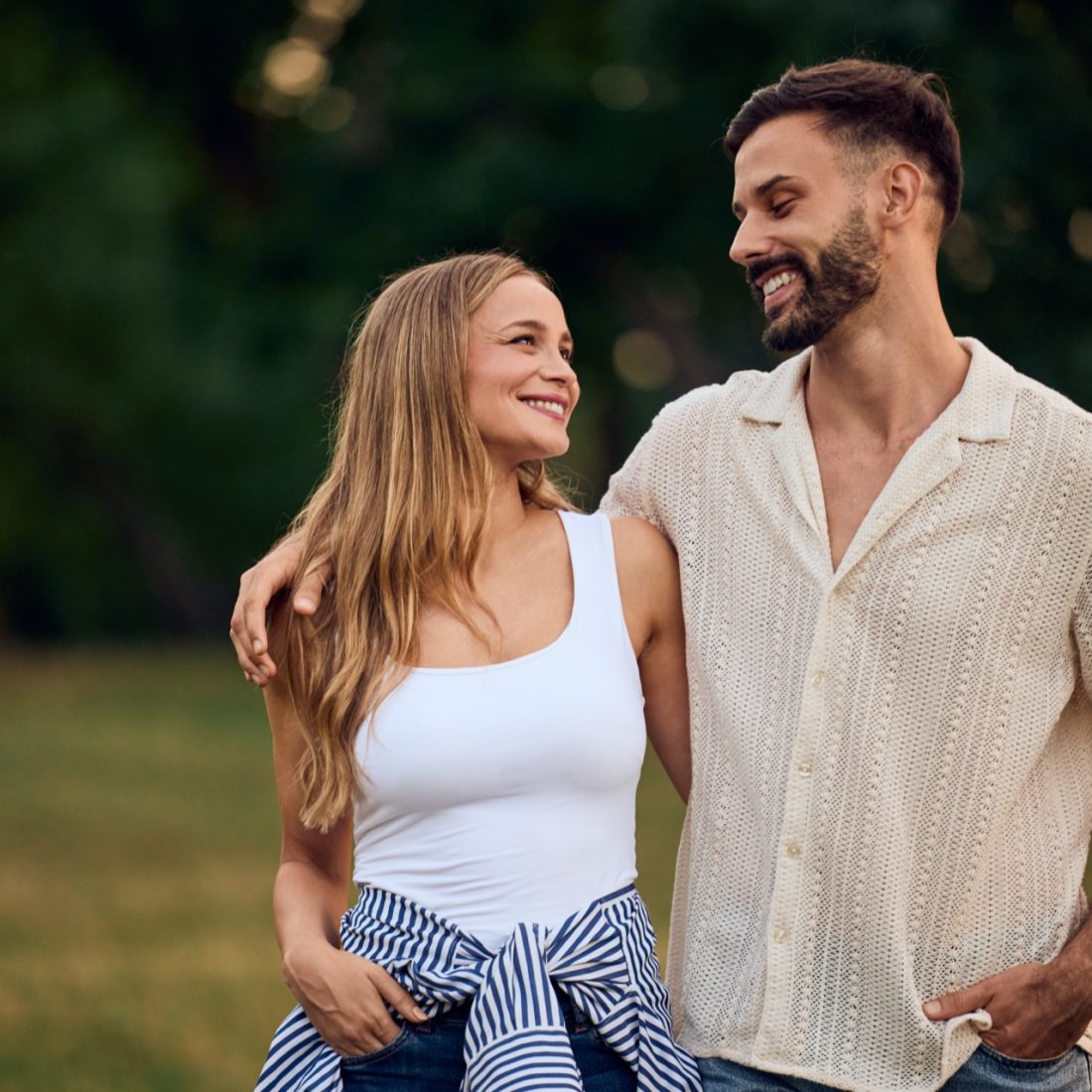 Two lovers walking through the park, smiling at each other, in a hug.